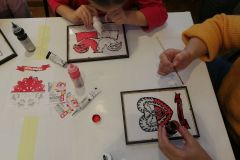 Dwoje dzieci tworzy biało-czerwone obrazki inspirowane wycinanką kurpiowską, techniką malowania na szkle
