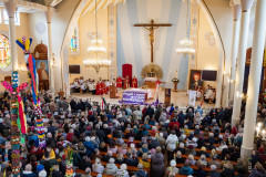 Uroczysta msza święta w Niedzielę palmową. Kościół wypełniony wiernymi. Niektórzy trzymają wysokie na kilka metrów palmy. Widok z chóru w kierunku  ołtarza. Z prawej strony widoczny obraz kardynała Stefana Wyszyńskiego.