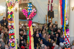 Uroczysta msza święta w Niedzielę palmową. Kościół wypełniony wiernymi. Widok z chóru na nawę boczną. Widoczne wysokie palmy.