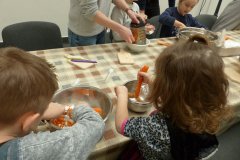 Dzieci siedzą przy stole i ucierają marchew.