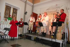 Grupa artystów gra koncert, kobieta przed nimi przemawia.