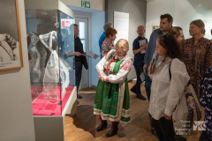 Kobieta w stroju kurpi białych opowiada o chuście kilku osobom 