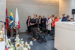 Stoją uczestnicy uroczystej mszy świętej odprawianej w krypcie Pomnika Mauzoleum. Z lewej strony w stojaku: flagi:  Polski, Województwa Mazowieckiego oraz Ostrołęki.