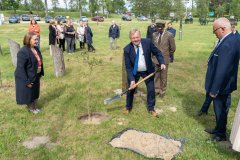 Uczestnicy uroczystości stoją przy alei bohaterów. Mężczyzna sadzi dąb.