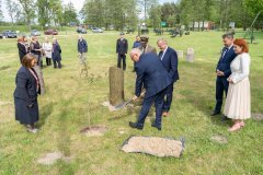 Uczestnicy uroczystości stoją przy alei bohaterów. Mężczyzna sadzi dąb.