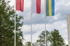 Trzy flagi na masztach. Po środku flaga Polski, z prawej strony flaga Miasta Ostrołęki, z lewej flaga województwa Mazowieckiego.