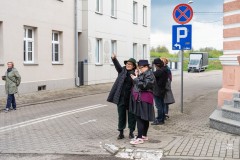 Kilka osób między budynkami starego miasta. Jedna z kobiet wskazuje dłonią w dal