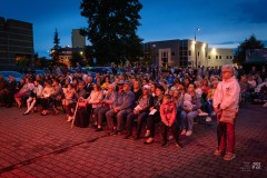 O zmroku ludzie siedzą na widowni w plenerze, pojedyncze osoby stoją