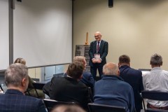 Mężczyzna stojąc przemawia do kilku osób siedzących na widowni