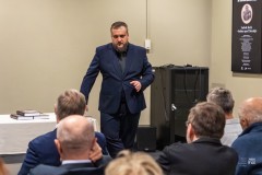 Mężczyzna stojąc przemawia do zgromadzomnych na widowni. Widoczne kilka osób