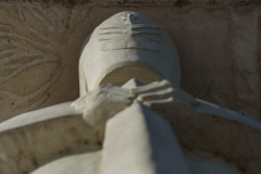 Fragment rzeźby żołnierza. Zdjęcie wykonane z dołu przy samej podstawie rzeźby, widoczne dłonie i czapka