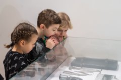 Dwie dziewczynki i chłopiec oglądają zabytki w szklanej gablocie na wystawie