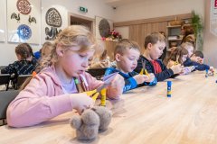 Dzieci siedząc przy stołach wykonują wycinankę kurpiowską