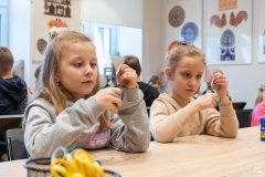 Dwie dziewczynki siedząc przy stole wykonują wycinankę kurpiowską.