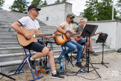 Trzej muzycy grający na gitarach, w tle schody Pomnika Mauzoleum.