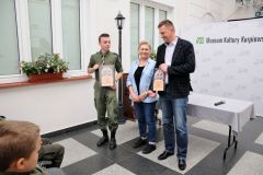 Dwóch prowadzących wręcza nagrodę harcerzowi.