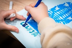 Dłonie wykonujące flamastrem napis LELUJA pod naklejoną na kartkę wycinanką