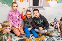Dzieci siedzą na podłodze. Chłopczyk unosi dłoń