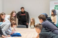 Uczestnicy lekcji historycznej rozwiązują przy stole karty edukacyjne