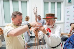 dwóch mężczyzn razem wyplata koszyk, w tle jest kilka osób