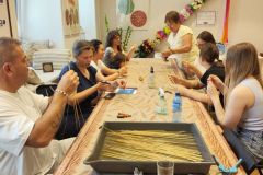 osiem osób przy wspólnym stole wykonuje ozdoby ze słomy