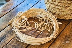 Na drewnianym blacie leży materiał do wyplatania zwinięty w koło