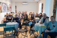 Duża grupa uczestników spotkania promocyjnego książkę słucha wypowiedzi autora książki.