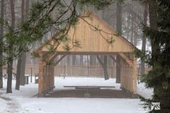 Drewniana konstrukcja budynku w trakcie budowy, w tle las, wokół śnieg.