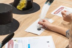 Dłoń mocząca końcówkę ptasiego pióra w plastikowym pojemniczku z atramentem
