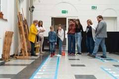 Dorośli i dzieci, uczestnicy imprezy patriotycznej w budynku Muzeum grają w grę przestrzenna.