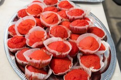 Kilkadziesiąt czerwonych ciastek (babeczek) w białych, papierowych foremkach, na metalowej tacy.