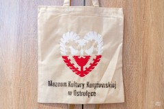 Tekstylna torba z namalowana biało-czerwoną wycinanką w kształcie serca i poniżej z czarnym napisem pod spodem Muzeum Kultury Kurpiowskiej w Ostrołęce