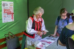 W namiocie kobieta w kurpiowskim stroju wykonuje wycinankę. Obok stoją uczestniczki warsztatów.