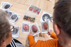 Kobieta i mężczyzna oglądają ilustracje pisanek wielkanocnych leżące na stole. Widok z za ramion