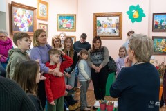 Kilkanaście osób, dorośli i dzieci, zwiedzają wystawę prac malarskich