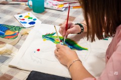 Dłonie osoby malującej kolorowe ptaki na płóciennej torbie