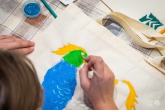 Dłonie osoby malującej kolorowe ptaki na płóciennej torbie