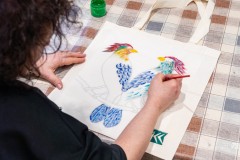 Dłonie osoby malującej kolorowe ptaki na płóciennej torbie