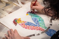 Dłonie osoby malującej kolorowe ptaki na płóciennej torbie