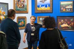 Mężczyzna i kobieta słuchają przewodniczki oprowadzającej ich po wystawie prac malarskich