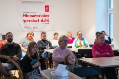 W ławkach siedzą uczestnicy spotkania – kilkanaście osób, w tym dzieci.
