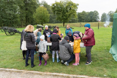 Uczestnicy pikniku Fortach Bema stojąc przy stole przy rozwiązują zadania na kartach edukacyjnych. W tle Skansen Artylerii