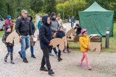 Uczestnicy pikniku na Fortach Bema idą z tekturowymi końmi na kiju. W tle jeden z namiotów