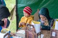 Dzieci – uczestnicy pikniku na Fortach Bema rozwiązują zadania na kartach edukacyjnych w jednym z namiotów