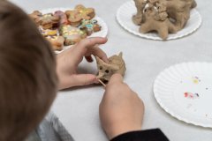 Na tle stołu dłonie dziecka na wykonującego byśka – pieczywo obrzędowe. W tle fragment gotowych byśków oraz zdobionych pierniczków