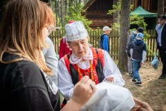 Kobieta w tradycyjnym stroju kurpiowskim demonstruje uczestniczce warsztatów wiązanie chystki na głowie