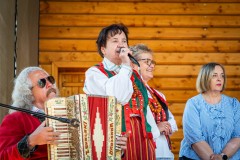 Kobieta w stroju kurpiowskim stojąc na scenie śpiewa do mikrofonu. Po jej prawej stronie siedzi mężczyzna w stroju kurpiowskim i gra na harmonii. Z jej lewej strony stoją dwie kobiety, jedna również w stroju kurpiowskim.
