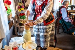 Kobietra w stroju kurpiowskim robi masło ze śmietany
