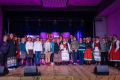 Mężczyzna oraz ponad trzydzieści kobiet pozują do wspólnego zdjęcia na scenie. Jedna z kobiet trzyma grawerton, niektóre są w stroju kurpiowskim.