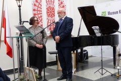 Mężczyzna stoi przy mikrofonie, fortepianie i obok stoi kobieta